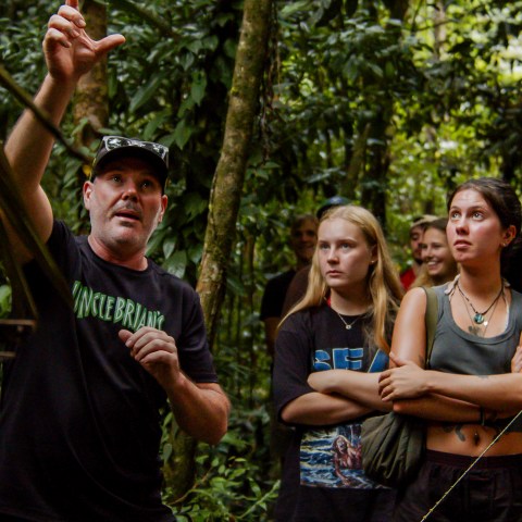 Guide explaining to a group of young adults in a lush forest setting.